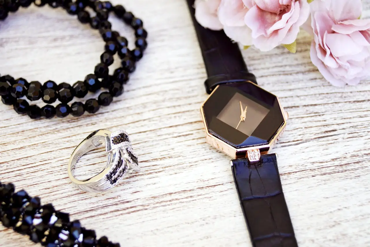 services-01 Close-up of luxurious black jewelry and watch with pink flowers on a wooden surface.
