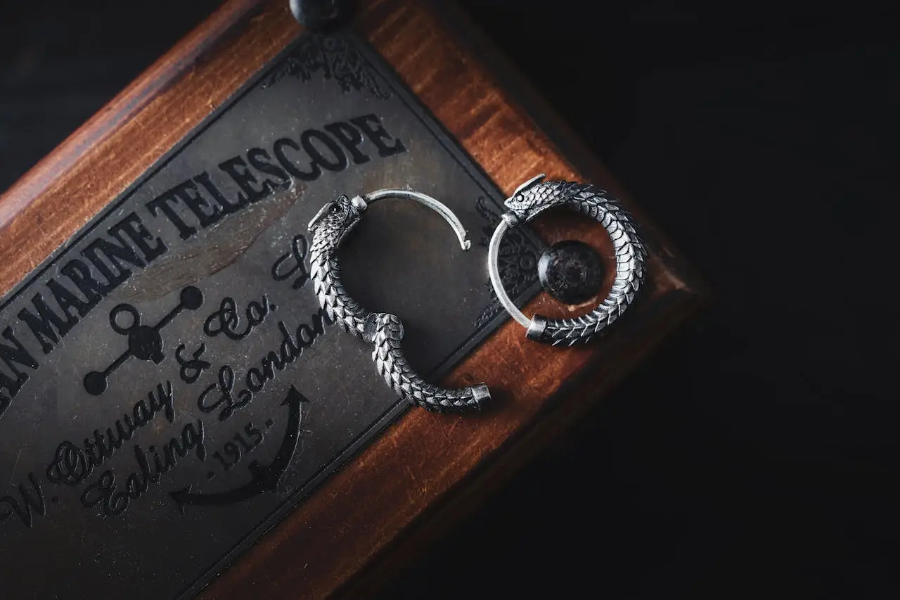 services-04 Artistic shot of silver ouroboros earrings on vintage telescopic box, perfect for jewelry lovers.
