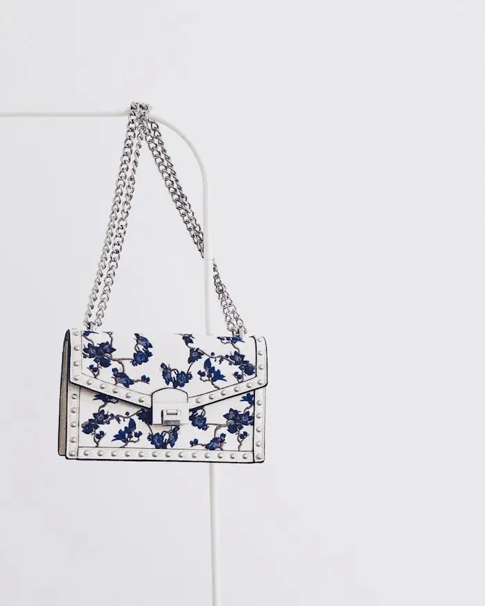 about-us Elegant white handbag with blue floral design and silver chain, perfect for fashion enthusiasts.